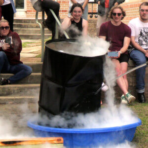 An audience watches in excitement as a black large drum is imploded from atmospheric pressure.