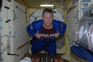 Col. Michael Fossum showing his Aggie shirt while floating without gravity aboard a space craft.