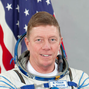 Col. Michael E. Fossum in his astronaut suit and the American flag in the background.