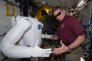 Col. Michael Fossum looks at the camera while posing next to a NASA robot.